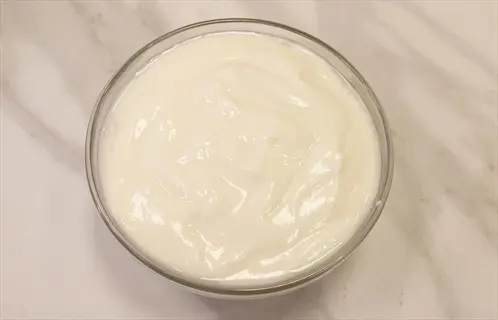 a glass bowl filled with plain yogurt on a marbled surface