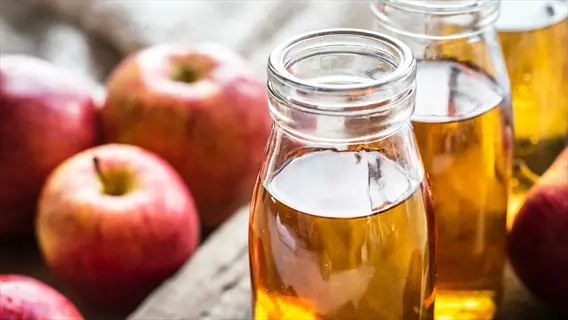 apple cider vinegar in glass bottles with fresh red apples on a rustic wooden surface