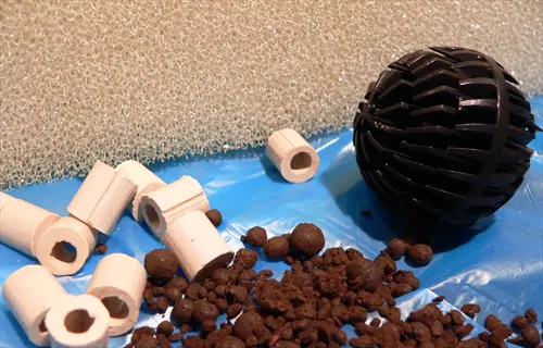 assorted aquarium filter media: ceramic rings, black spherical bio-ball, and clay pellets for biological filtration