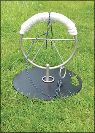 bird perch rotation training apparatus: circular metal frame with padded perch, rope attachments, and ring target on weighted black base, positioned on grassy field