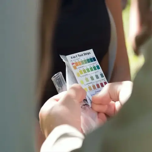 closeup of hands holding 4-in-1 aquarium test strips package and test tube with visible color scale chart