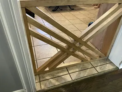 wide pet safety gate: geometric wooden barrier installed in doorway - blocks access to tiled kitchen area with visible feet of person beyond